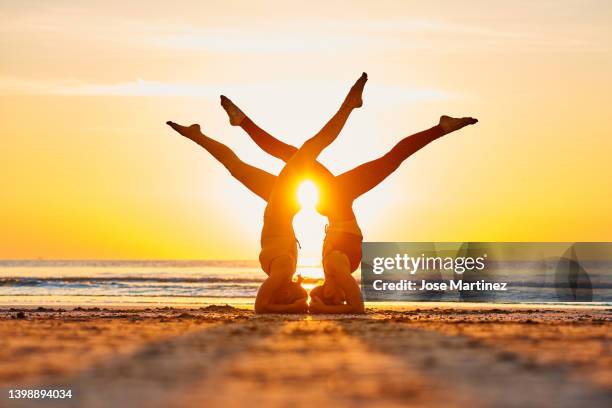 two women doing yoga on the beach at sunrise in the  sirsasana pose - shirshasana stock pictures, royalty-free photos & images