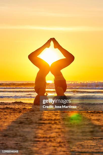 two women doing yoga on the beach at sunrise in the  sirsasana pose - shirshasana stock pictures, royalty-free photos & images