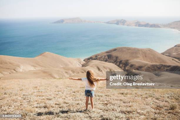 toddler girl on hill with amazing coastline and sea view. summer mood, view from behind - girl mound stock pictures, royalty-free photos & images