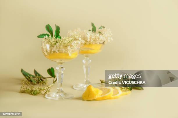 summer cocktails with elder flowers and lemon slices  in champagne glasses at pale yellow background. - limonade stockfoto's en -beelden