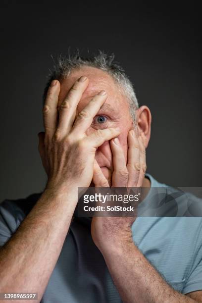 mature adult peaking his eye through his hands - odd one out obscure stock pictures, royalty-free photos & images