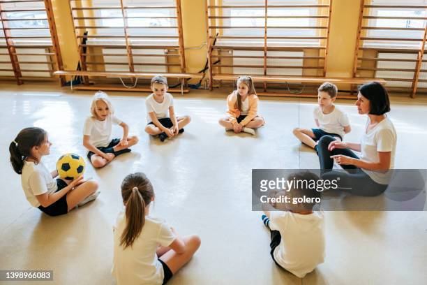 bambini delle scuole elementari seduti in cerchio in palestra con l'insegnante - bambini seduti in cerchio foto e immagini stock