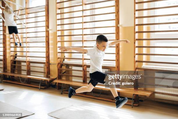 elementary schoolboy jumping in gym - physical education stock pictures, royalty-free photos & images