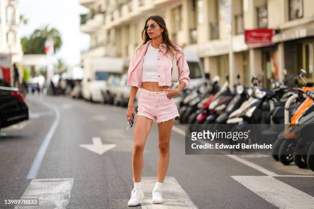 Julia Sidi Atman wears sunglasses, a white t-shirt / crop top, a pastel colored pink denim ripped crop jacket with short puffy sleeves, pink ripped...