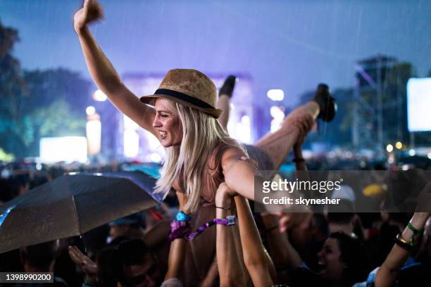 young cheerful woman held by her friends during rainy night on music festival. - rock music festival stock pictures, royalty-free photos & images