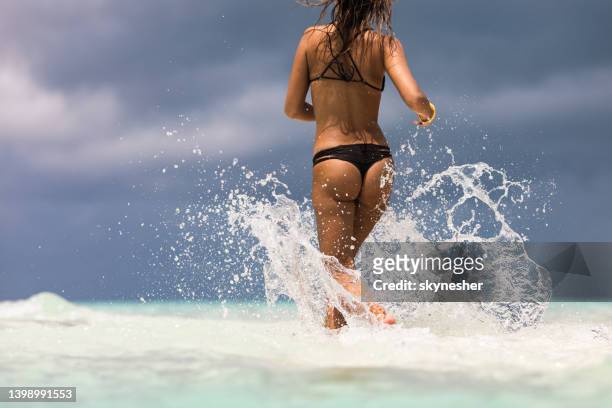 vista para trás de uma mulher de biquíni correndo pelo mar. - tanga - fotografias e filmes do acervo