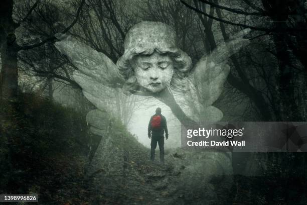 a mystery concept of a hiker lost in a spooky winters forest. with a double exposure of a graveyard angel over the top. with a grunge, vintage edit. - angel statue stock-fotos und bilder
