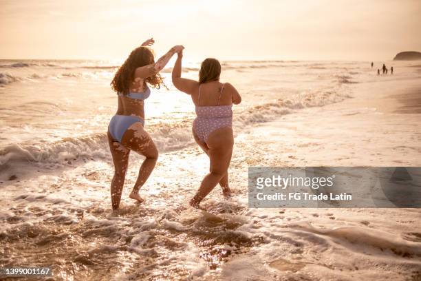 junge freundinnen, die am strand spazieren gehen - dicke frauen am strand stock-fotos und bilder