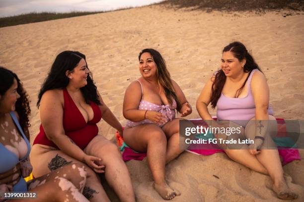 female friends sitting on the sand and talking on the beach - latin beauty stockfoto's en -beelden