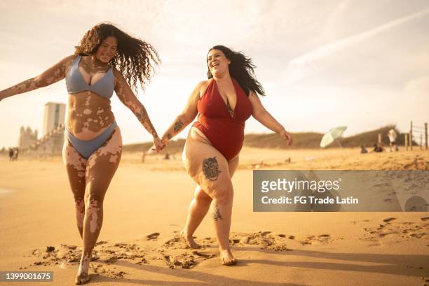 amigos tomados de la mano caminando por la playa - beautiful plump women fotografías e imágenes de stock