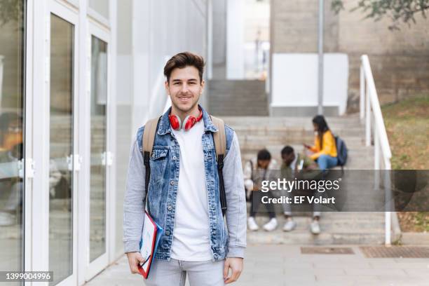 portrait of handsome male university student. smiling man with denim jacket standing at the college campus - modern boy hipster stock pictures, royalty-free photos & images