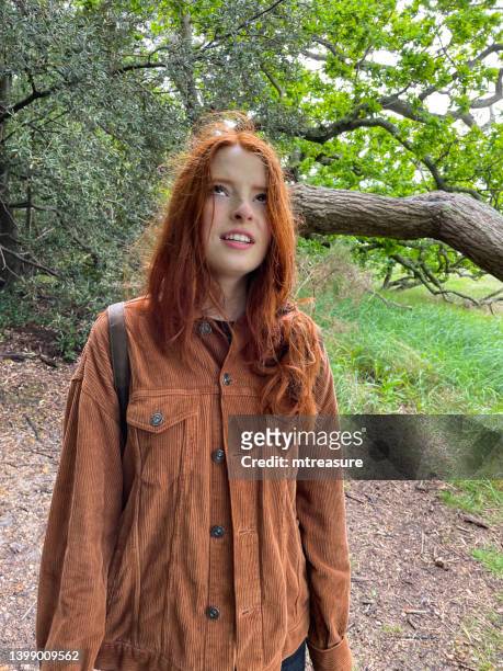 image of attractive, red haired young woman stood looking to the sky, english oak tree (quercus robur) trunk on woodland floor, storm damage, focus on foreground - corduroy stockfoto's en -beelden