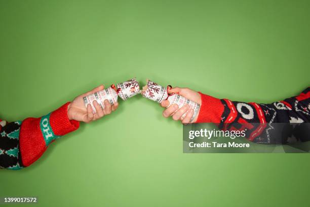 christmas cracker being pulled by two people wearing christmas sweaters - christmas crackers stock pictures, royalty-free photos & images