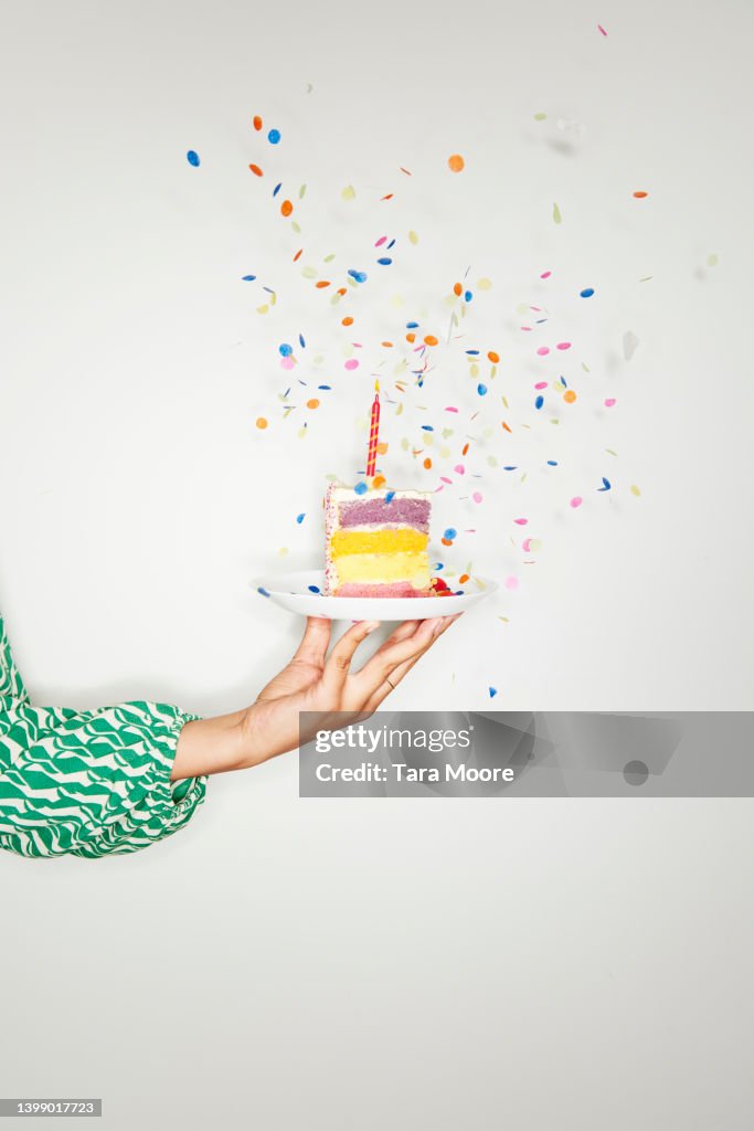 Hand holding birthday cake with confetti