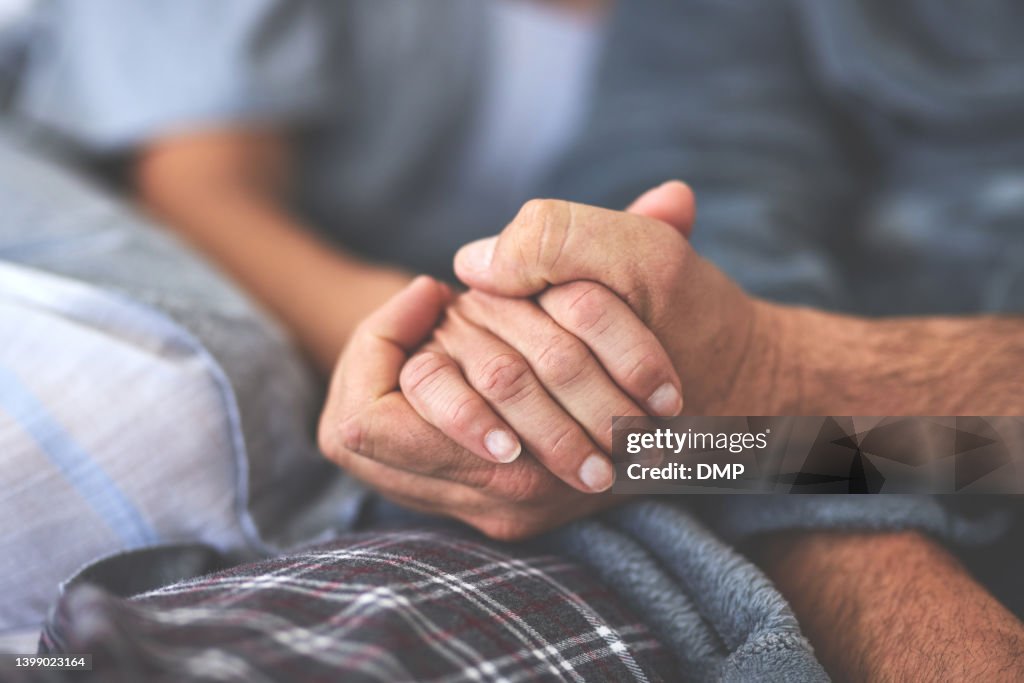 A couple holding hands in bed at home. Closeup of a happy man and woman in love, relaxing in the bedroom during the morning, sharing a romantic moment