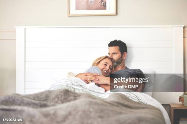 a couple relaxing in bed at home. a happy mature man and woman in love, cuddling in the bedroom during the morning, sharing a romantic moment - good morning kiss images 個照片及圖片檔