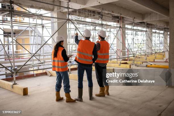 three workers (architects, engineers) examining building site - construccion fotografías e imágenes de stock