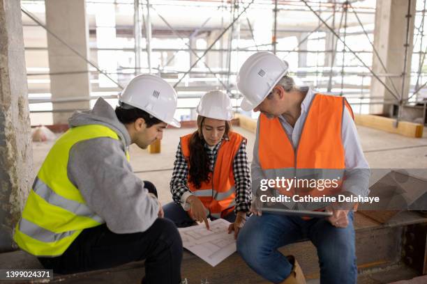 three workers discussing and looking at plans as they visiting a building site - foundations gender equality discussion stock-fotos und bilder