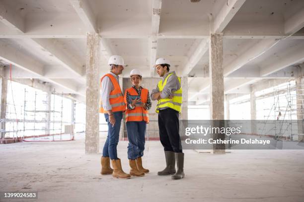 three workers discussing and looking at a digital tablet as they visiting a building site - foundations gender equality discussion stock-fotos und bilder