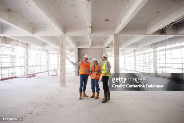 three workers discussing and looking at a digital tablet as they visiting a building site - foundations gender equality discussion stock-fotos und bilder