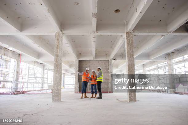 three workers discussing and looking at a digital tablet as they visiting a building site - foundations gender equality discussion stock pictures, royalty-free photos & images