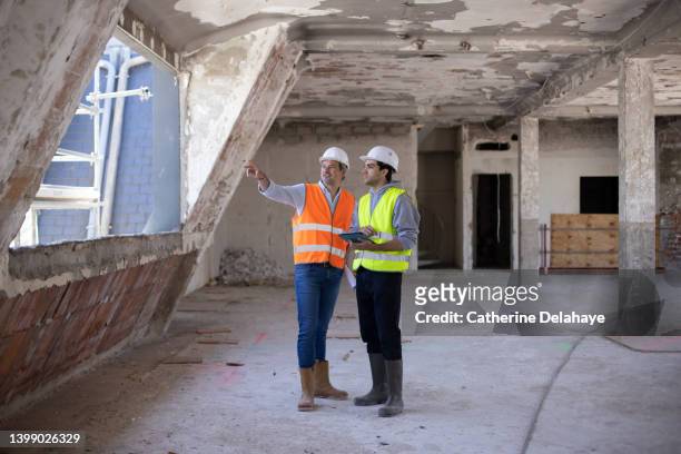two workers discussing and looking at a digital tablet as they visiting a building site - digital techniques ストックフォトと画像