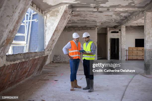 two workers discussing and looking at a digital tablet as they visiting a building site - hard hat ipad stock pictures, royalty-free photos & images