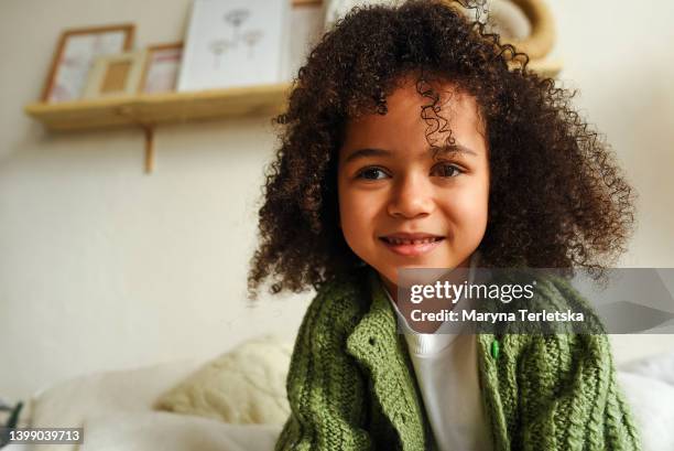 dark-skinned baby girl sits on the bed. casual style. curly black hair. cute afro girl. - curly brown hair stock pictures, royalty-free photos & images