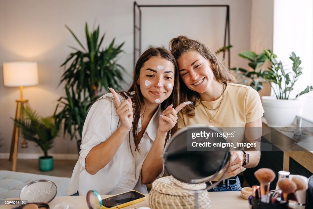 Two happy girls applying make up at home