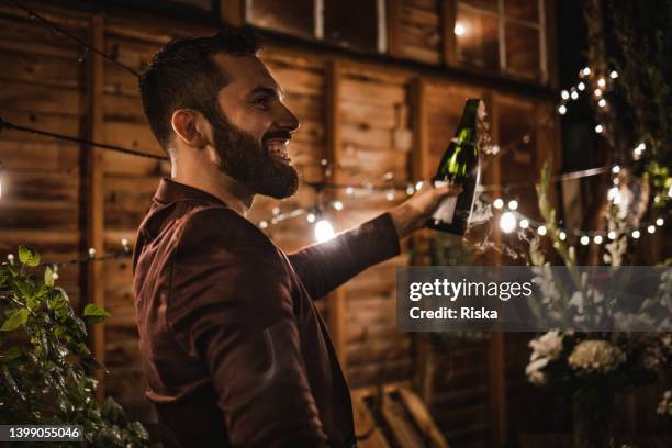 the groom is opening a bottle of champagne - opening night of bright star arrivals stockfoto's en -beelden