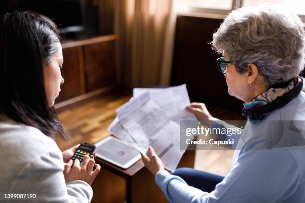consultant calculating numbers while seeing bills being showed by elder lady - denial stock pictures, royalty-free photos & images