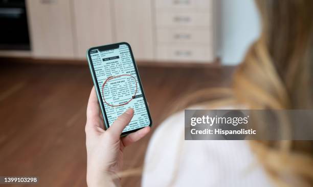 woman looking at a real estate classified online on her phone - newspaper ad stock pictures, royalty-free photos & images