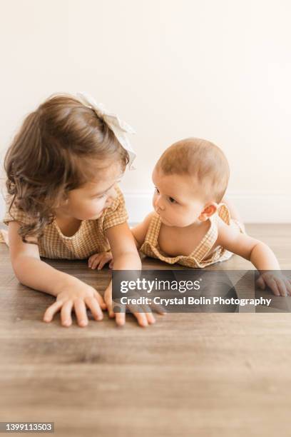 a 3-year-old toddler girl and her 5-month-old baby brother looking at each other while laying on their bellies on the floor for tummy time while wearing matching yellow plaid outfits - baby girl laying on tummy stock pictures, royalty-free photos & images