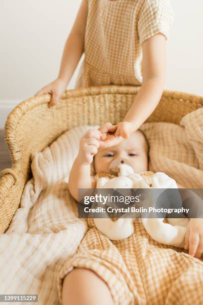 uma menina de 3 anos de idade de mãos dadas com seu irmão bebê de 5 meses enquanto ele deita em uma cesta de moisés - vestido cor de pele - fotografias e filmes do acervo