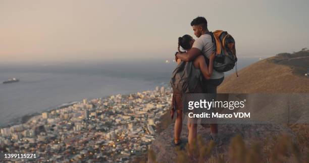 a couple hiking up a mountain on a travel adventure. rear view of a young man and woman in love looking at the view while exploring nature at sunset - summer romance stock pictures, royalty-free photos & images