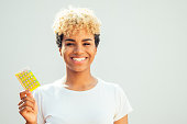 brazilian girl with cute afro blonde curls showing contraceptive pills in studio white background