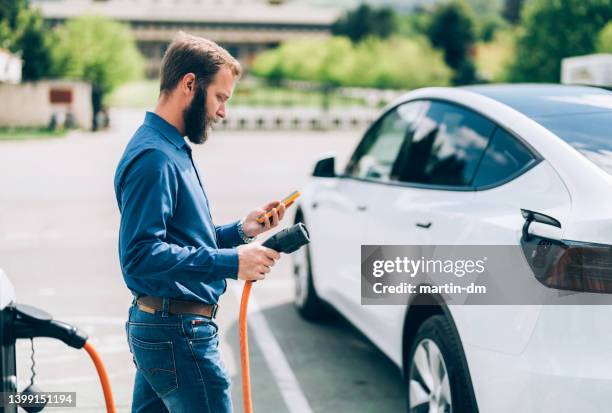 man charging electric car - electric vehicle charging station stock pictures, royalty-free photos & images