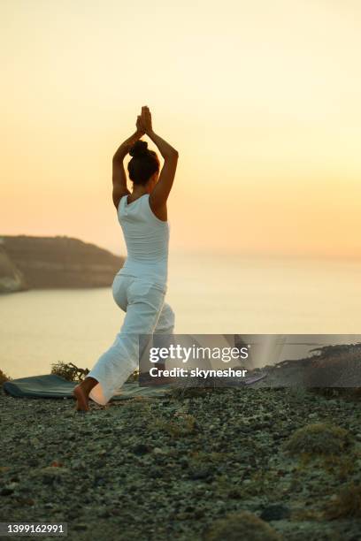 back view of female athlete exercising yoga on a hill at sunrise. - sunrise yoga stock pictures, royalty-free photos & images