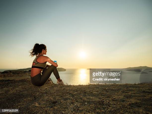 athlète féminine prenant une pause aquatique sur une colline au-dessus de la mer. - groyne photos et images de collection