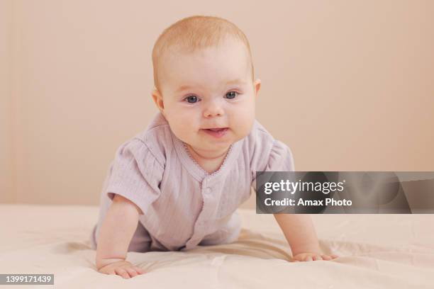 smiling little baby girl with big blue eyes lying on her tummy on the bed at home - baby girl laying on tummy stock pictures, royalty-free photos & images