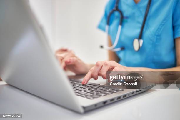 close-up hands of unrecognizable female physician in medical uniform working typing on laptop keyboard sitting at desk - doctor laptop stock pictures, royalty-free photos & images