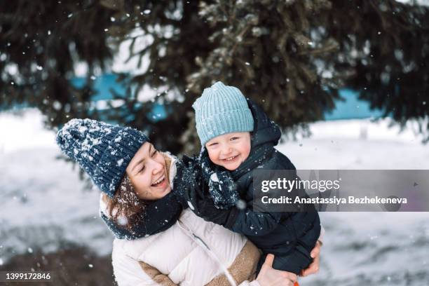 mom and son in front of the christmas trees against the backdrop of falling snow - baby christmas stock-fotos und bilder