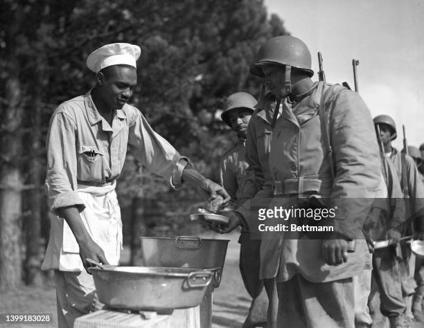 Mess Sargeant John Black of Jackson, Mississippi, former chef at the Robert E. Lee Hotel in Jackson Mississippi, gives food to Private Buck Ellington...