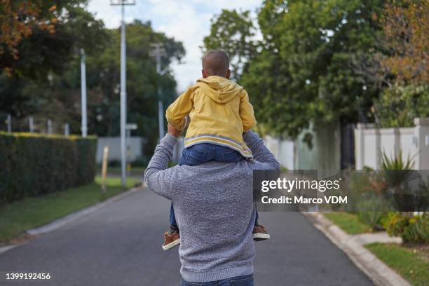 padre e hijo caminando por la calle. vista trasera de un hombre maduro llevando a su hijo pequeño por la carretera, divirtiéndose y disfrutando de un paseo al aire libre - llevar al hombro fotografías e imágenes de stock