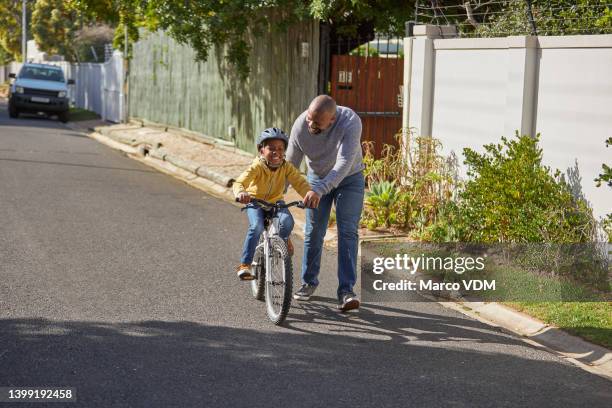 little boy riding a bicycle with his father. a mature father and his son learning to ride a bike outdoors. cute little boy and his dad having fun family time in the street - riding stockfoto's en -beelden