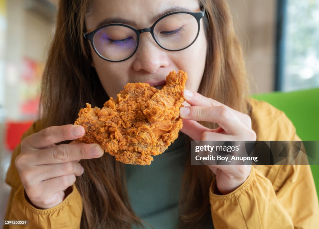 Cropped shot of young Asian woman while eating a piece of crispy fried chicken.