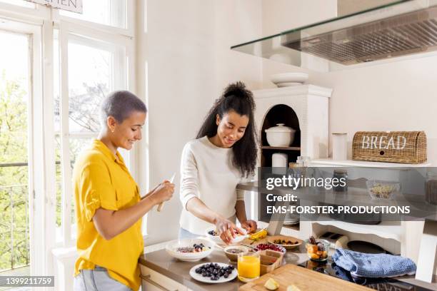 two young woman preparing healthy breakfast in modern kitchen - cutting green apple stock pictures, royalty-free photos & images