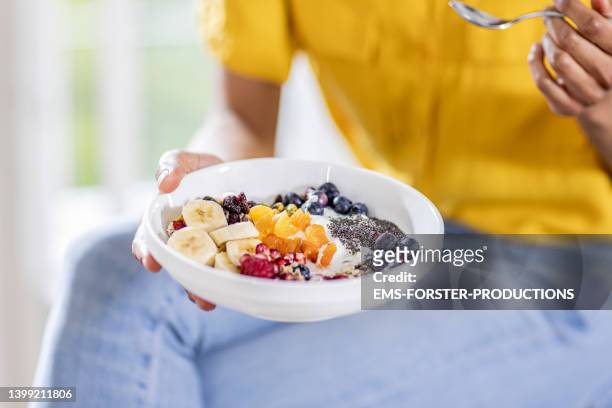 close up of beautiful student eating a fresh bowl with various fruits,  berries with chia seeds and nuts - same person different outfits stock-fotos und bilder