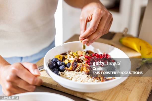 young woman is preparing her own bowl with fruits and nuts for breakfast - low carb diet stock pictures, royalty-free photos & images