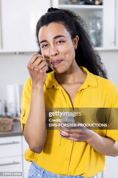 young and beautiful student eating yogurt at home - spoon in hand stock-fotos und bilder